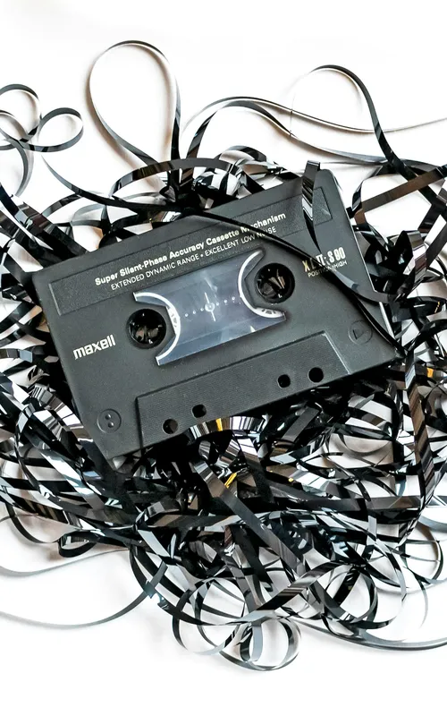 Schwarze Maxell-Audiokassette, deren Magnetband chaotisch auf weißem Untergrund aufgerollt ist